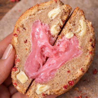 Cookie with pink filling held by a hand on a brown surface